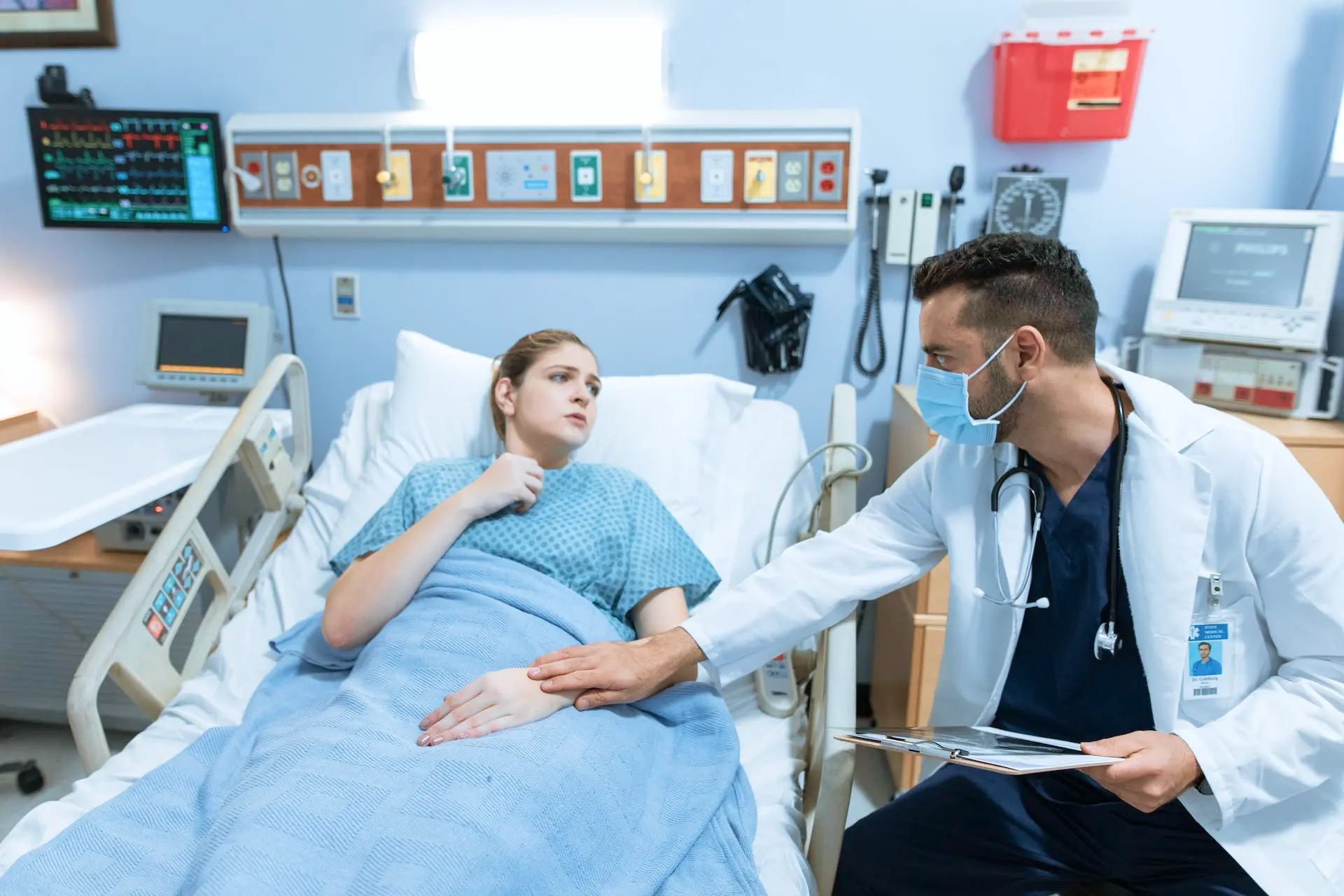 A male doctor holding hands of a woman sick in a hospital bed